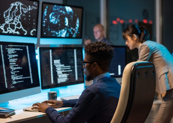 Young it-engineer decoding data while sitting in front of computer monitors and looking at screen of one of them
